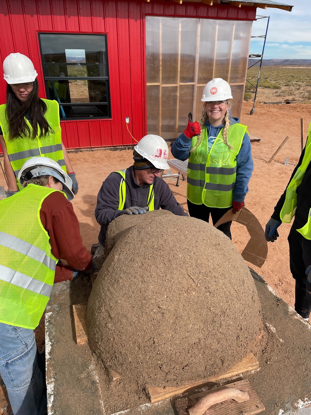 Students and community members shaping an earthen dome together