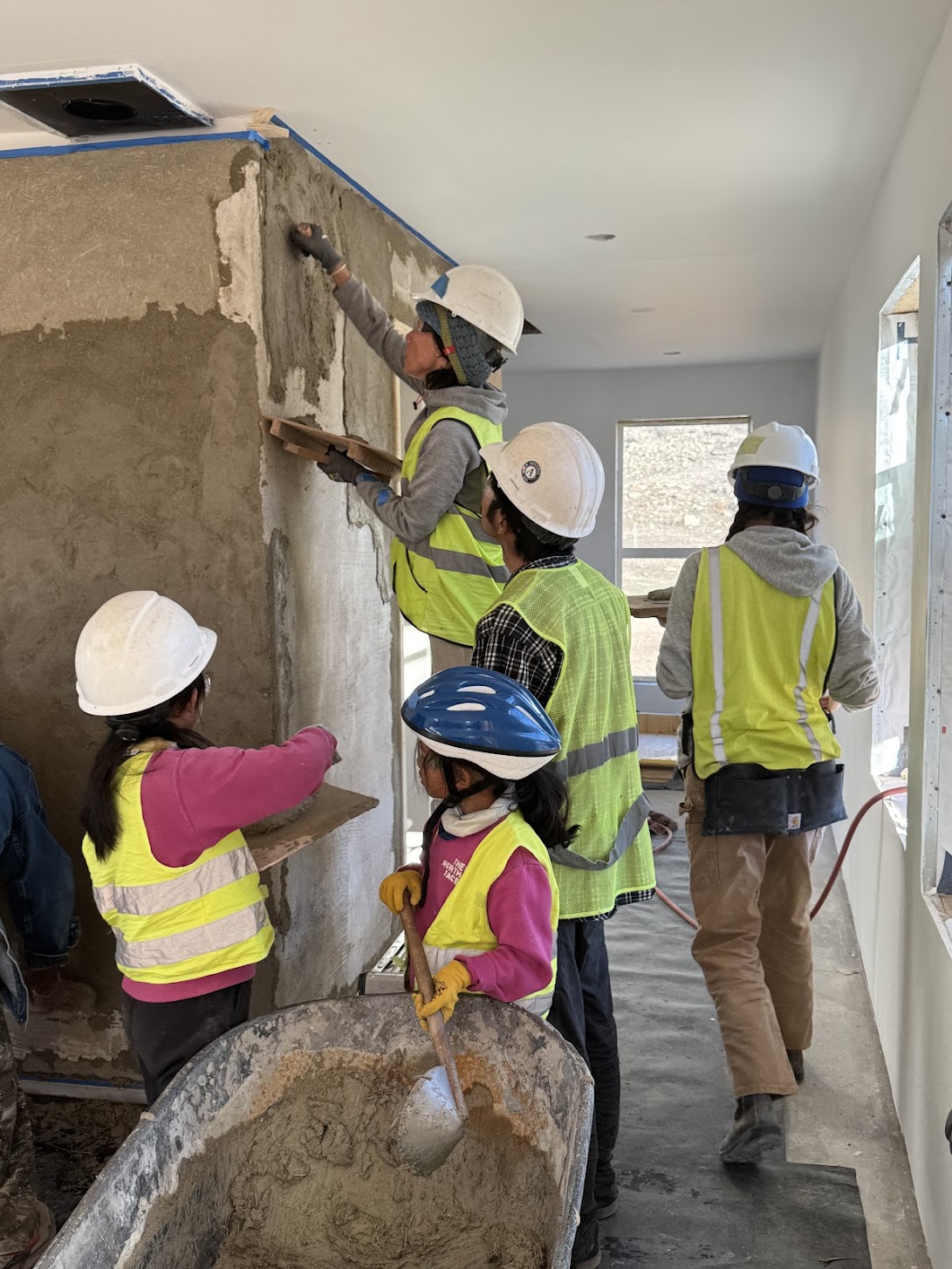 Adults and children plastering an earthen wall side by side