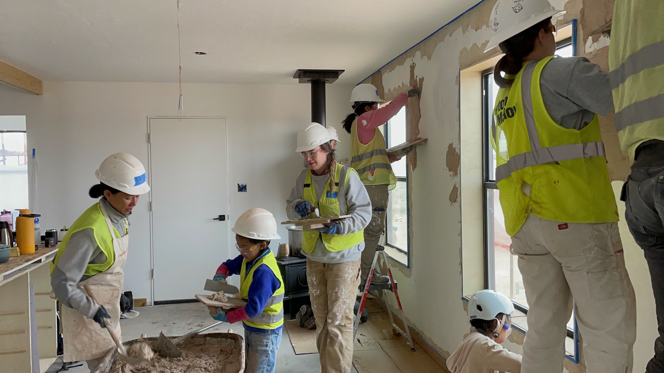 Students, families, and children plastering interior walls together